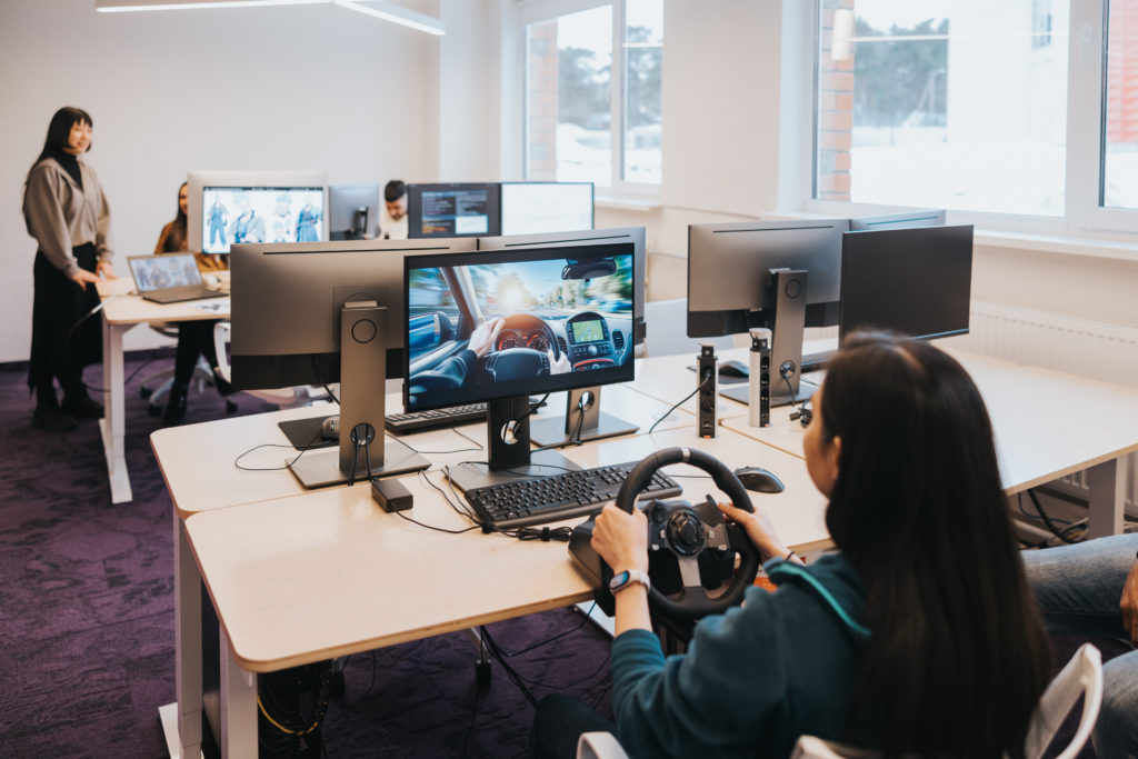 Female gaming designer takes charge of the driving simulator, showcasing her expertise as she navigates through the virtual world she and her team have crafted