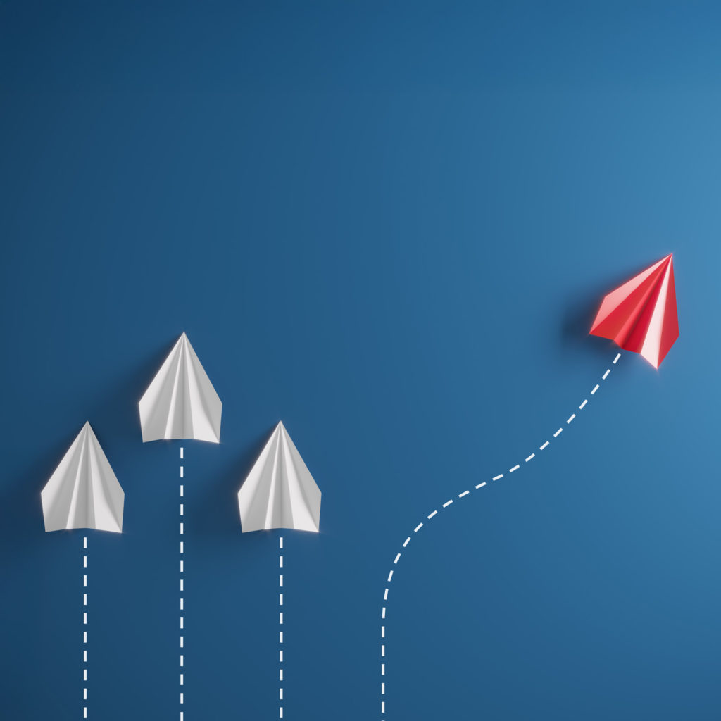 The illustration shows three white paper aeroplanes flying straight ahead and a red aeroplane creatively deviating from its course. It symbolises critical thinking, new perspectives and thinking outside the box.